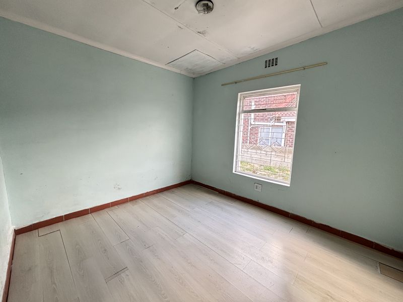 An empty bedroom featuring light-toned laminate flooring, pale blue walls, and a window fitted with security bars.