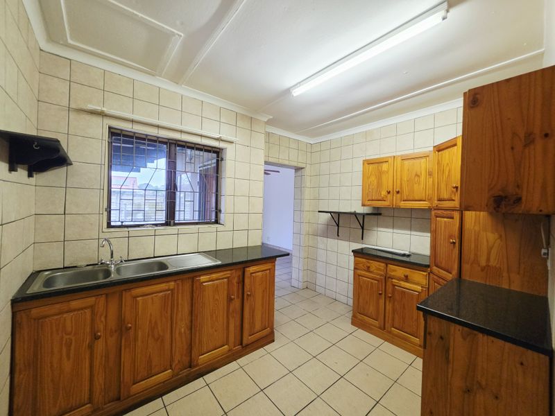 A functional kitchen featuring wooden cabinetry, double basin sink, tiled splashbacks, and tiled flooring, offering a clean space ready for modernization.