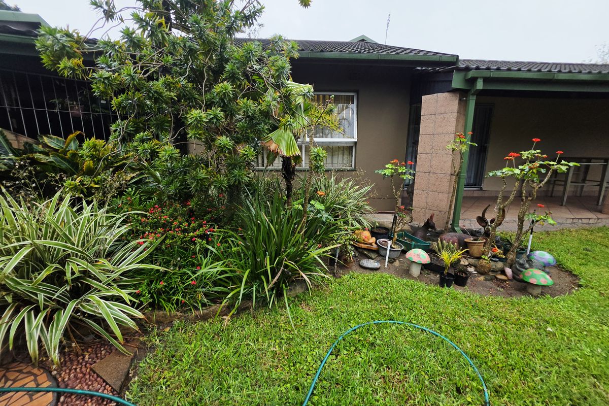 A view of the rear garden and patio area featuring established landscaping, a tiled roof, and a covered outdoor living space.