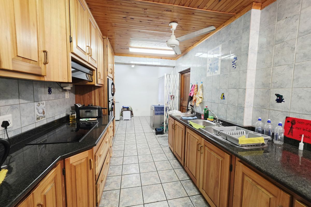 A functional galley-style kitchen featuring wooden cabinetry, granite countertops, built-in appliances, and a distinctive wooden ceiling with a ceiling fan.