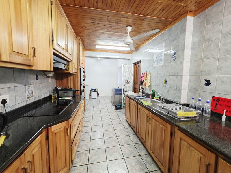A functional galley-style kitchen featuring wooden cabinetry, granite countertops, built-in appliances, and a distinctive wooden ceiling with a ceiling fan.
