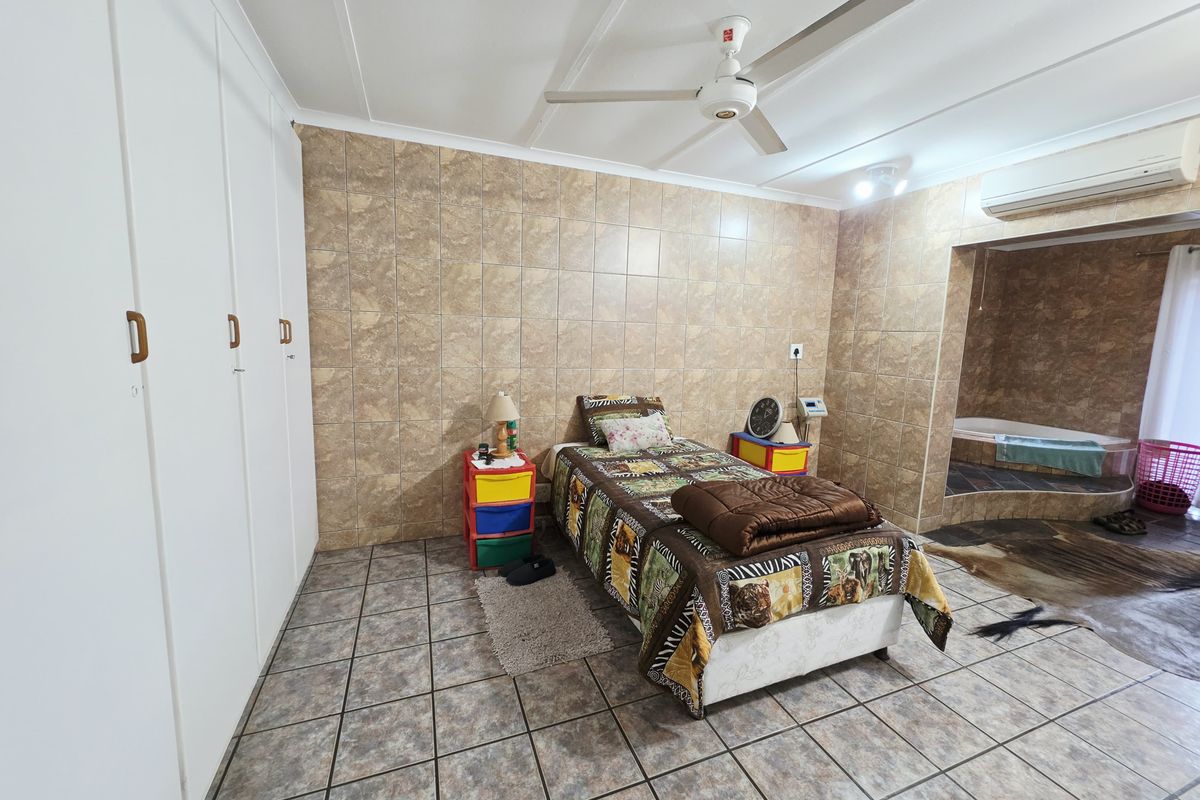 Spacious bedroom featuring built-in cupboards, tiled walls and flooring, a ceiling fan, air conditioning, and an integrated en-suite bathtub area.