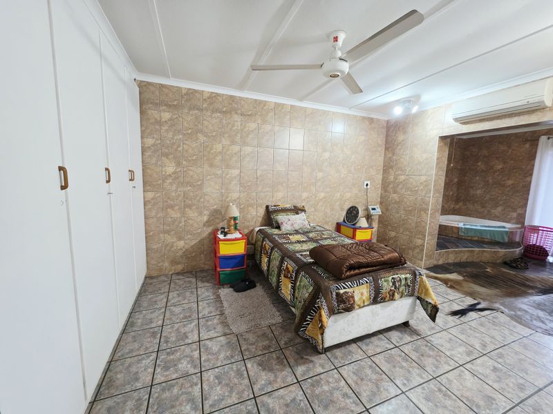 Spacious bedroom featuring built-in cupboards, tiled walls and flooring, a ceiling fan, air conditioning, and an integrated en-suite bathtub area.