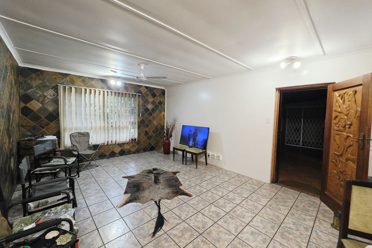 Spacious living room featuring tiled flooring, a stone accent wall, ceiling fan, and a decorative carved wooden door leading to an adjacent area.