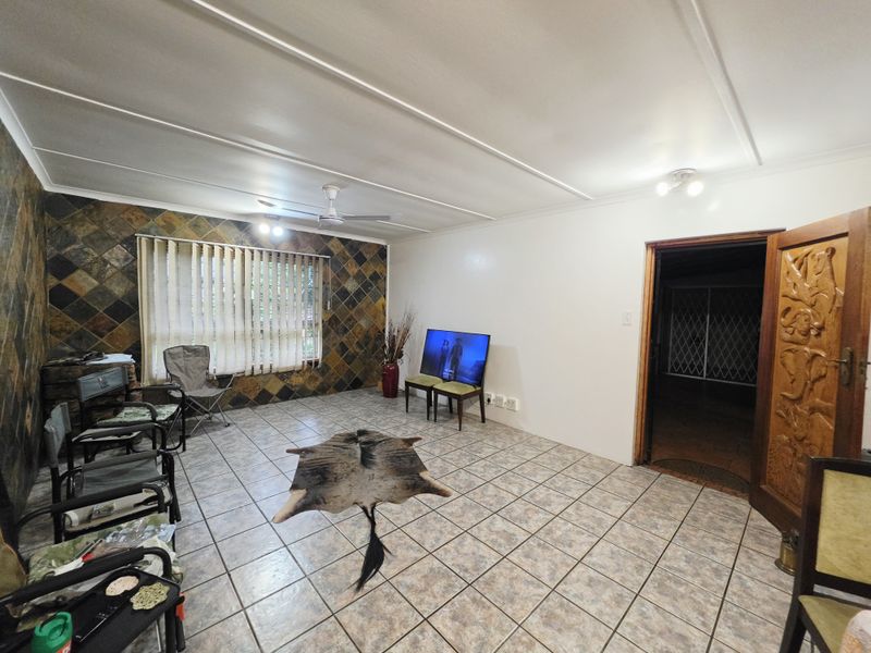 Spacious living room featuring tiled flooring, a stone accent wall, ceiling fan, and a decorative carved wooden door leading to an adjacent area.