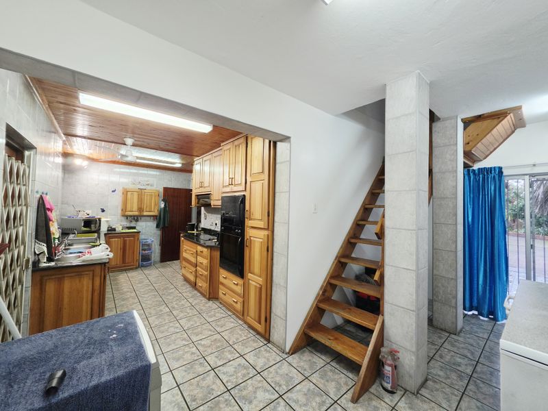 A functional kitchen featuring wooden cabinetry, built-in oven, and tiled flooring, with an adjacent wooden staircase leading to an upper level.