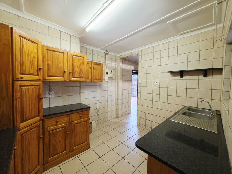 A functional kitchen featuring wooden cabinetry, granite countertops, a double stainless steel sink, and fully tiled walls and floors.