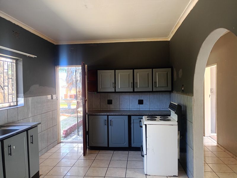 A functional kitchen featuring grey cabinetry, tiled splashbacks, and a freestanding stove, with direct access to the exterior through a security door.