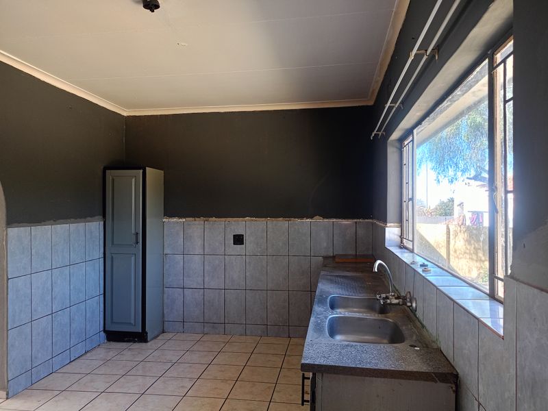 A functional kitchen space featuring a double stainless steel sink, tiled splashbacks, and tiled flooring, currently awaiting final finishes and cabinetry completion.