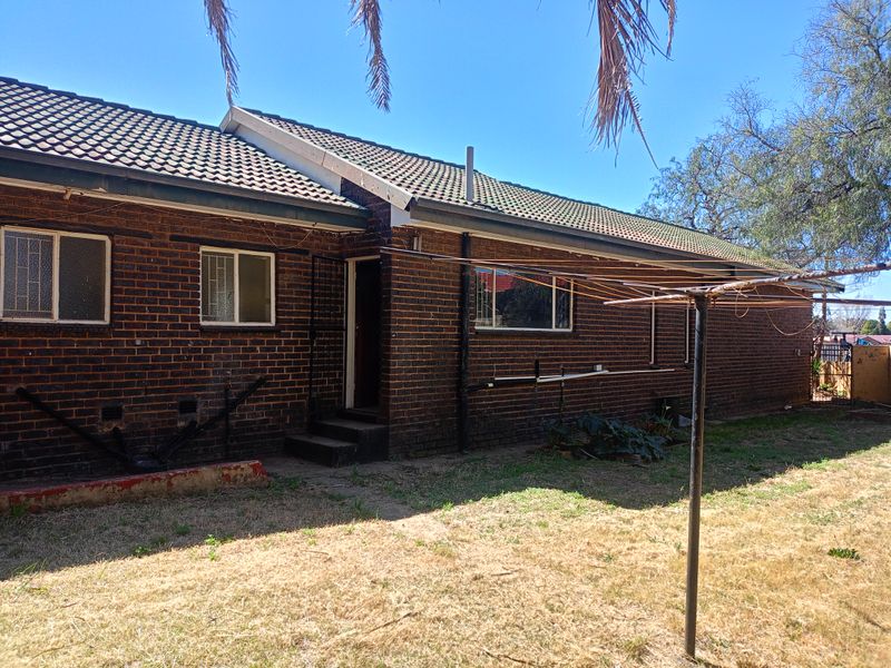 Rear view of a brick house featuring a tiled roof, concrete steps, and a large rotary clothesline set in a dry garden area.