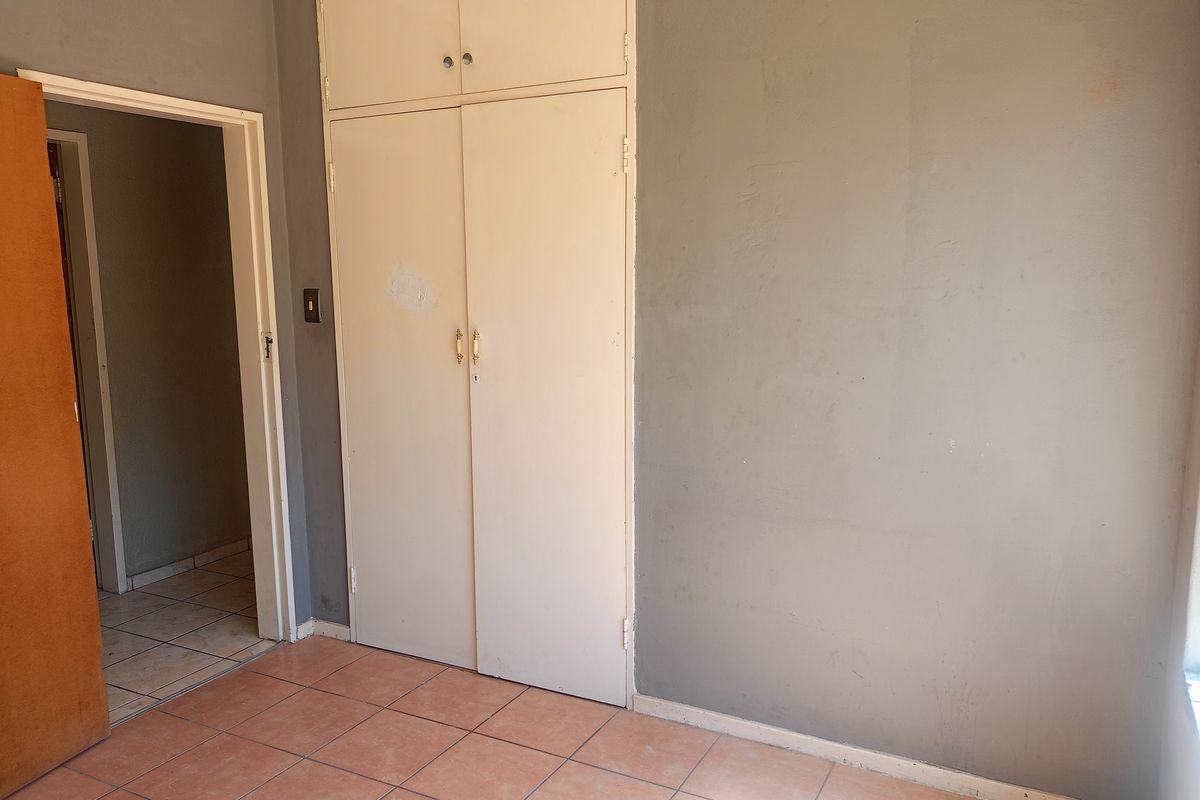 A vacant bedroom featuring tiled flooring and a built-in wardrobe, requiring minor cosmetic updates to the wall finishes.