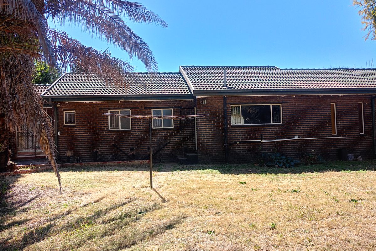 Rear view of a single-story brick house featuring a tiled roof, security bars on windows, and a large backyard with a rotary clothesline.