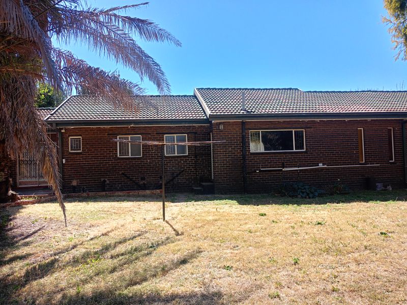 Rear view of a single-story brick house featuring a tiled roof, security bars on windows, and a large backyard with a rotary clothesline.