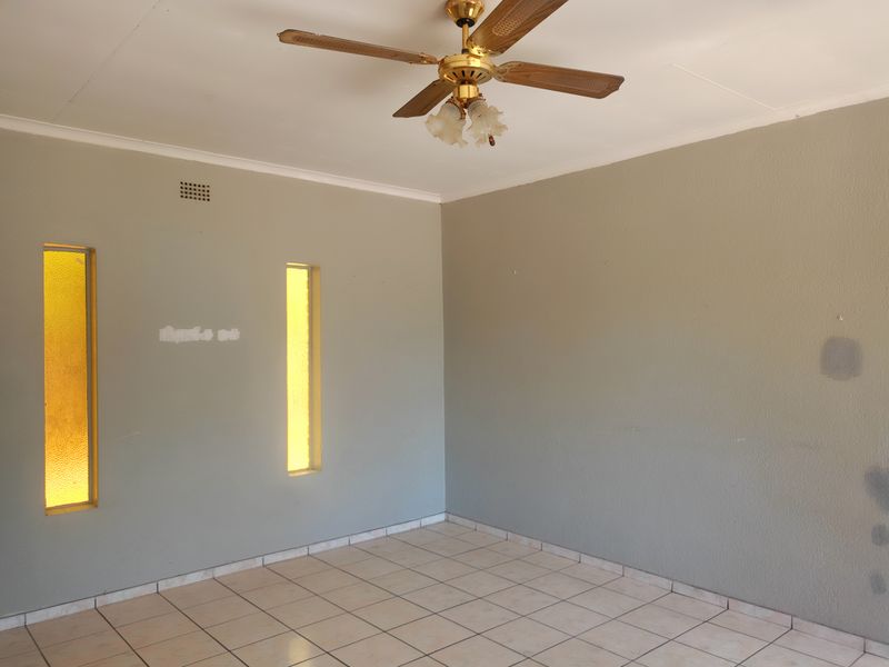 An empty living room featuring tiled flooring, a ceiling fan, and unique vertical windows, requiring minor cosmetic wall repairs.
