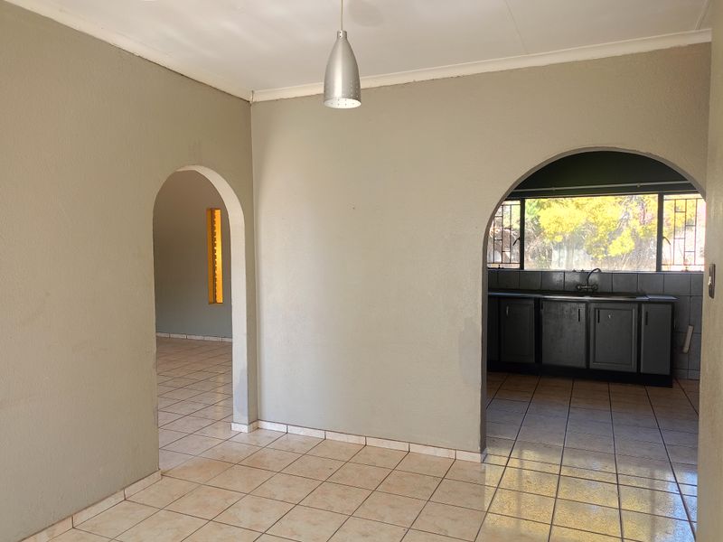 An empty open-plan living area featuring tiled floors, arched architectural transitions, and a view into the adjacent kitchen space.