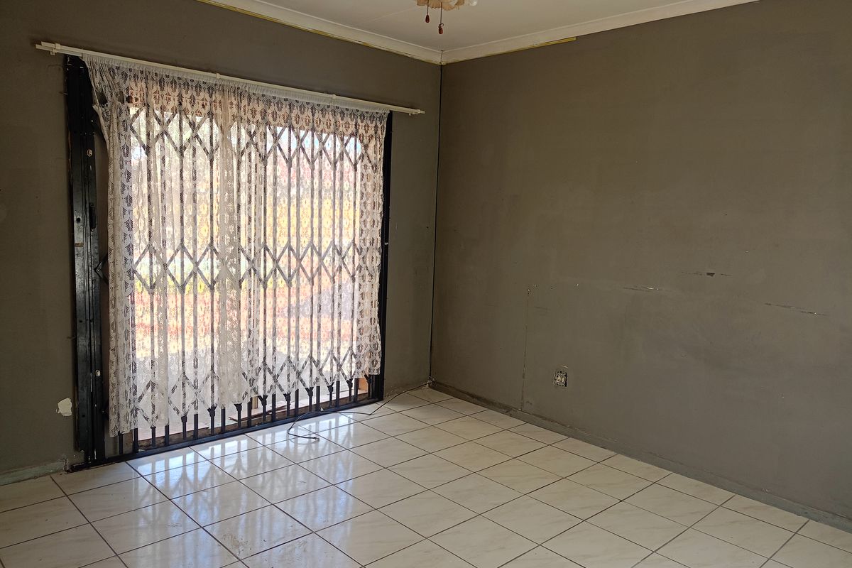 An empty living room featuring ceramic floor tiles, a ceiling fan, and a sliding glass door with a security gate.