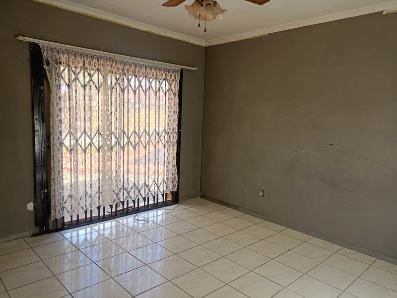 An empty living room featuring ceramic floor tiles, a ceiling fan, and a sliding glass door with a security gate.