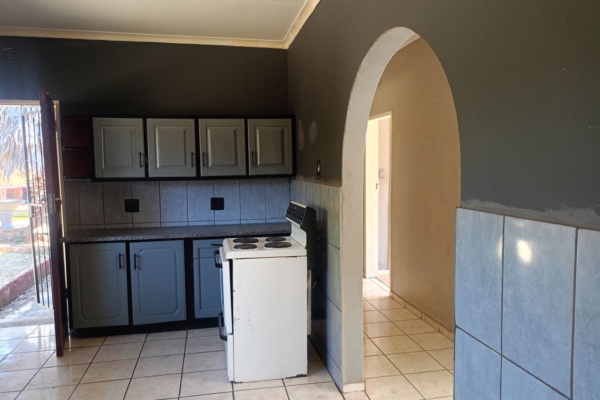 A functional kitchen featuring grey cabinetry, tiled backsplash, and a freestanding stove, connected to an adjacent hallway via a classic arched doorway.