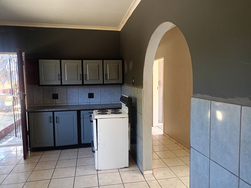 A functional kitchen featuring grey cabinetry, tiled backsplash, and a freestanding stove, connected to an adjacent hallway via a classic arched doorway.