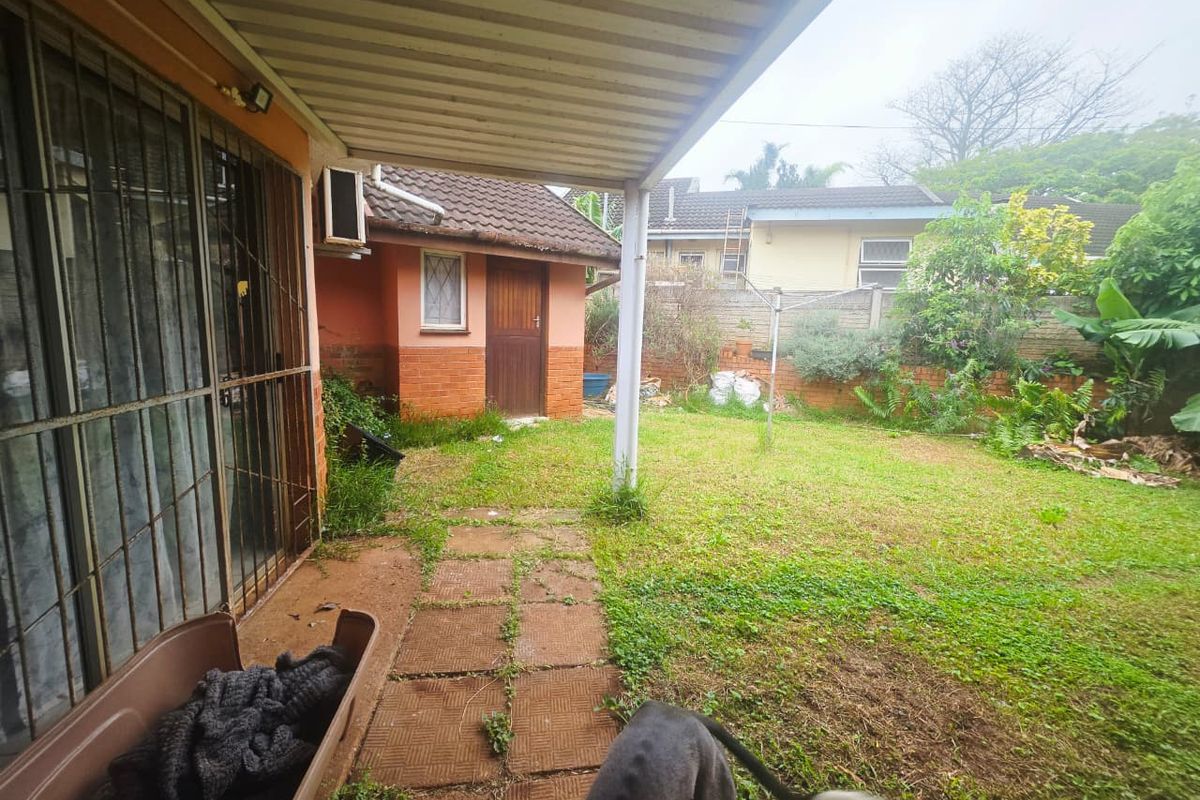 Rear exterior view featuring a covered patio, brick paving, and a garden area with established landscaping and brick boundary walls.
