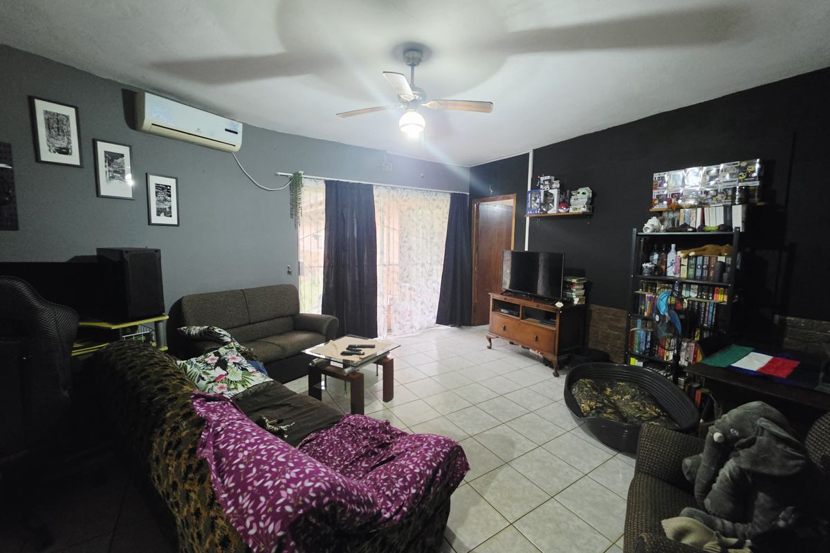 A living room featuring tiled flooring, a ceiling fan, and a wall-mounted split-system air conditioner with access to an outdoor area via sliding glass doors.