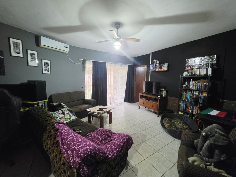 A living room featuring tiled flooring, a ceiling fan, and a wall-mounted split-system air conditioner with access to an outdoor area via sliding glass doors.