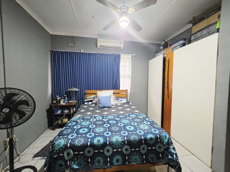 A functional bedroom featuring tiled flooring, a ceiling fan, a wall-mounted air conditioning unit, and built-in wardrobe storage.