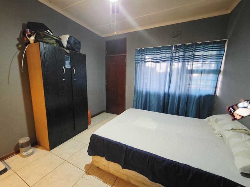 A bedroom featuring tiled flooring, a ceiling fan, and a built-in cupboard, providing a functional living space.