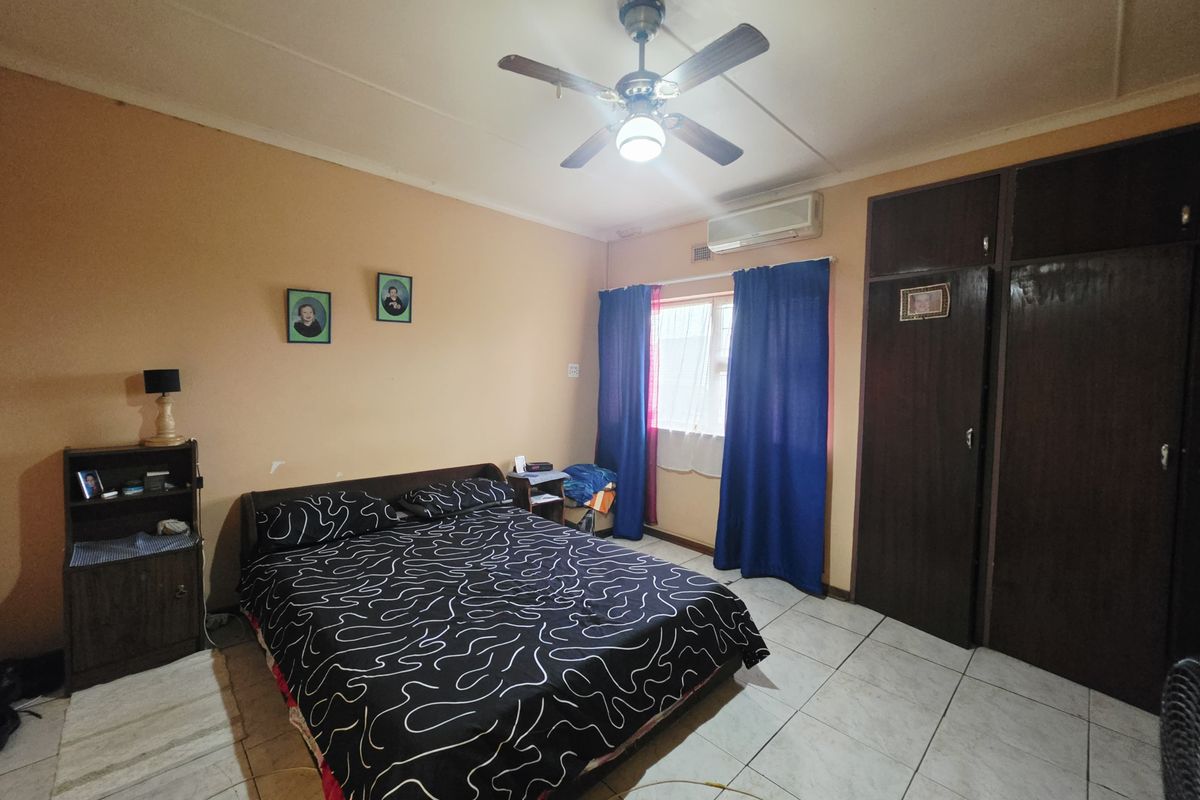 A functional bedroom featuring tiled flooring, built-in cupboards, a ceiling fan, and a wall-mounted air conditioning unit.