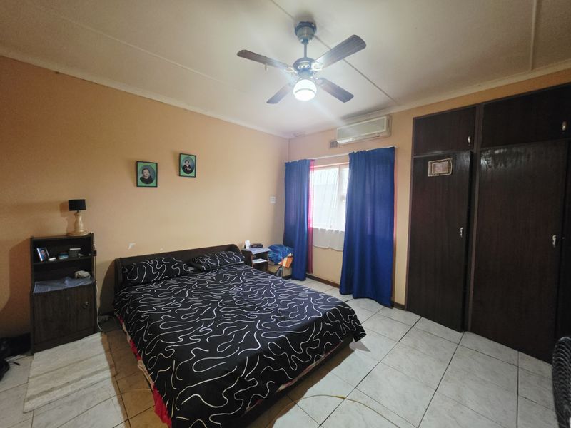 A functional bedroom featuring tiled flooring, built-in cupboards, a ceiling fan, and a wall-mounted air conditioning unit.