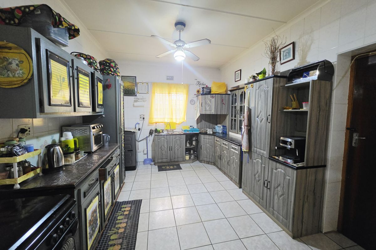 A functional kitchen featuring extensive built-in cabinetry, laminate countertops, tiled flooring, and a ceiling fan, offering a practical layout for daily meal preparation.