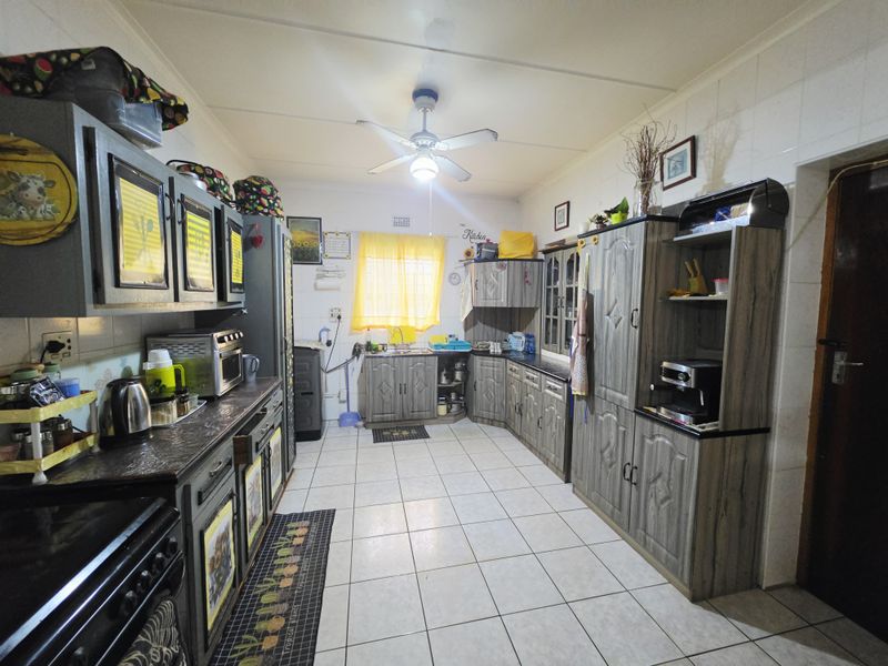 A functional kitchen featuring extensive built-in cabinetry, laminate countertops, tiled flooring, and a ceiling fan, offering a practical layout for daily meal preparation.