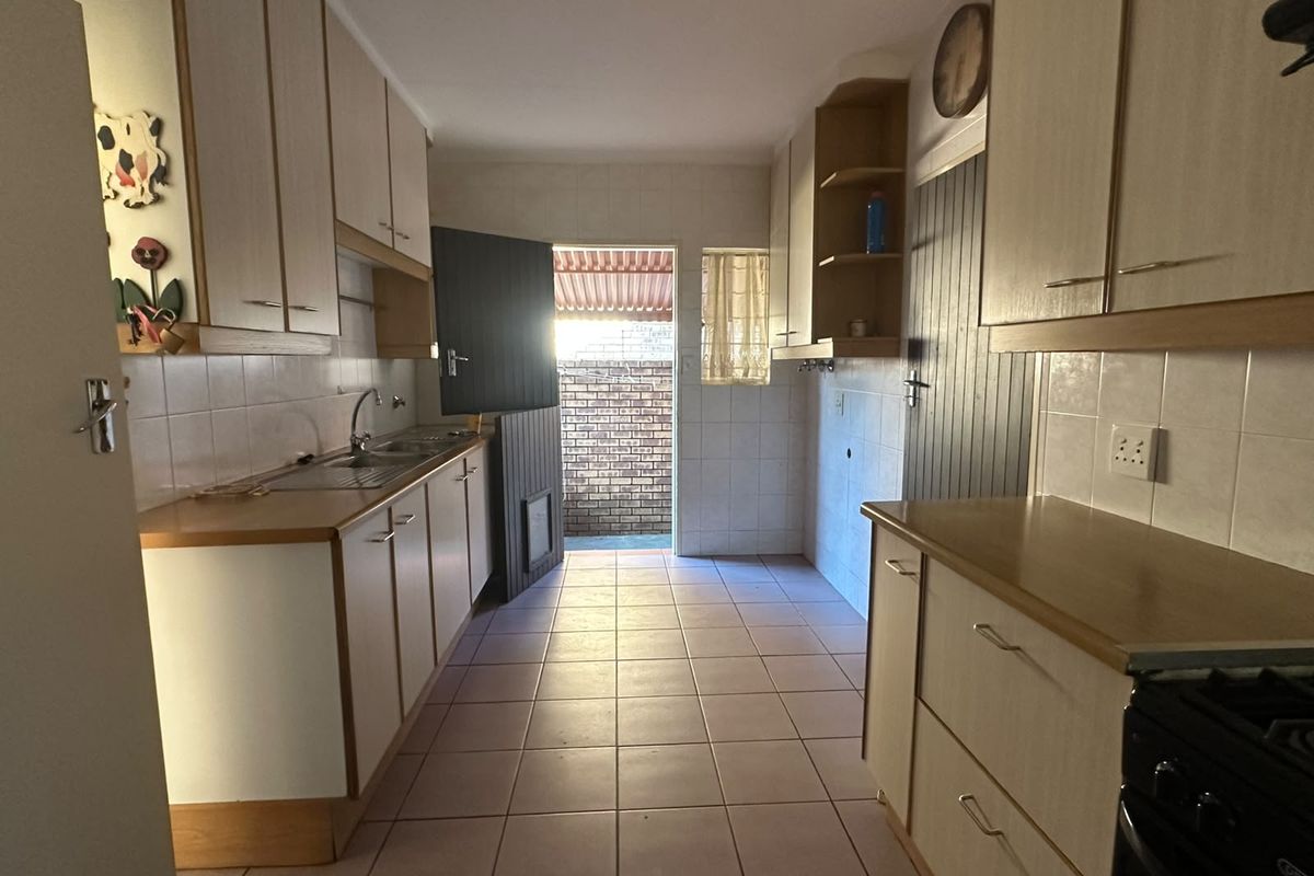 A functional kitchen featuring laminate cabinetry, tiled flooring, and a tiled backsplash, with direct access to an outdoor area.