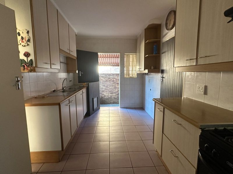 A functional kitchen featuring laminate cabinetry, tiled flooring, and a tiled backsplash, with direct access to an outdoor area.