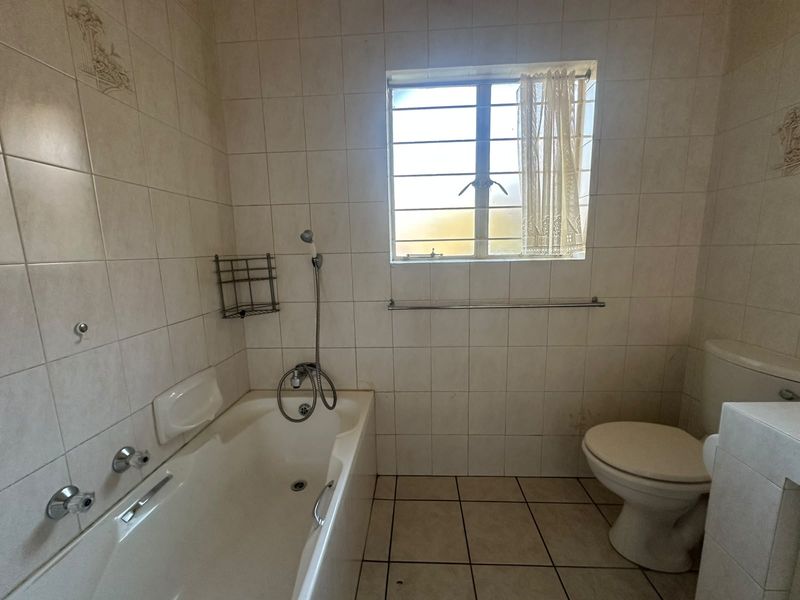 A functional bathroom featuring a bathtub with shower mixer, toilet, and neutral wall and floor tiling, offering potential for modernization.