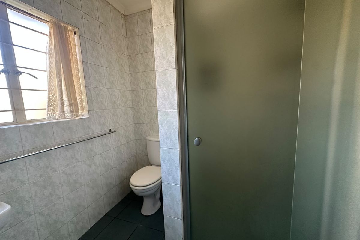 A functional bathroom featuring a toilet, shower enclosure, and tiled finishes. The space is dated and would benefit from modern updates.