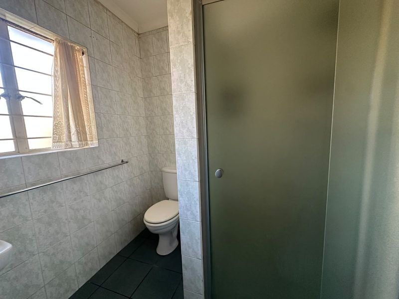 A functional bathroom featuring a toilet, shower enclosure, and tiled finishes. The space is dated and would benefit from modern updates.