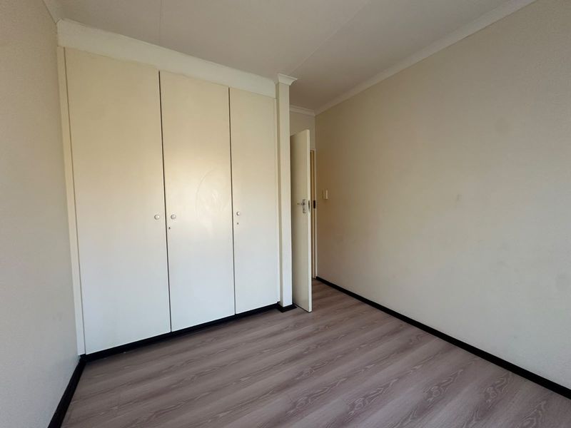 A clean, empty bedroom featuring neutral walls, laminate flooring, and built-in storage cupboards.