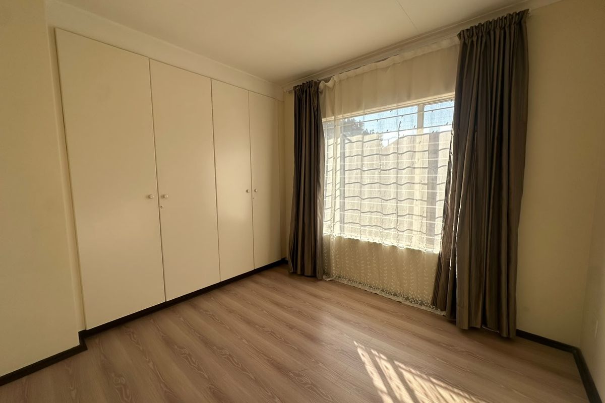 A clean, empty bedroom featuring light-toned laminate flooring and ample built-in cupboard storage space.