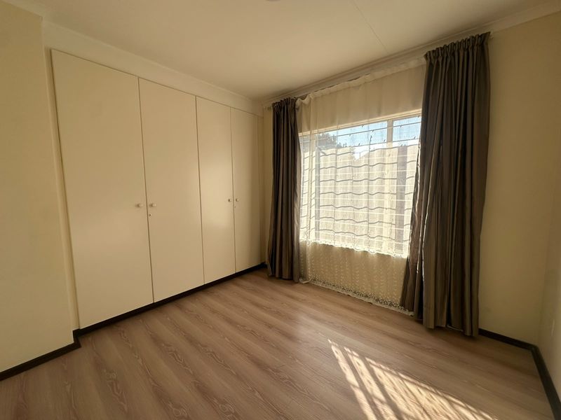 A clean, empty bedroom featuring light-toned laminate flooring and ample built-in cupboard storage space.