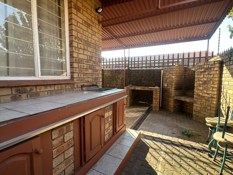 Covered outdoor patio area featuring a built-in brick braai, tiled prep counter with sink, and durable brick paving.