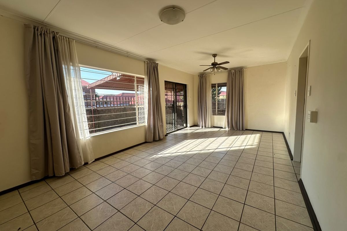 Spacious, sunlit living area featuring neutral tiled flooring, a ceiling fan, and large windows providing ample natural light.