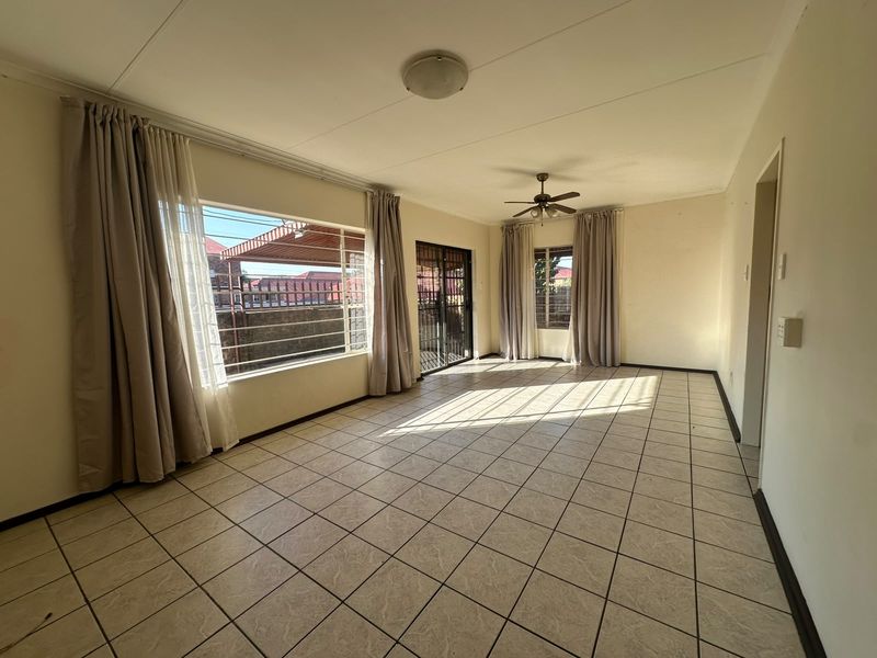 Spacious, sunlit living area featuring neutral tiled flooring, a ceiling fan, and large windows providing ample natural light.