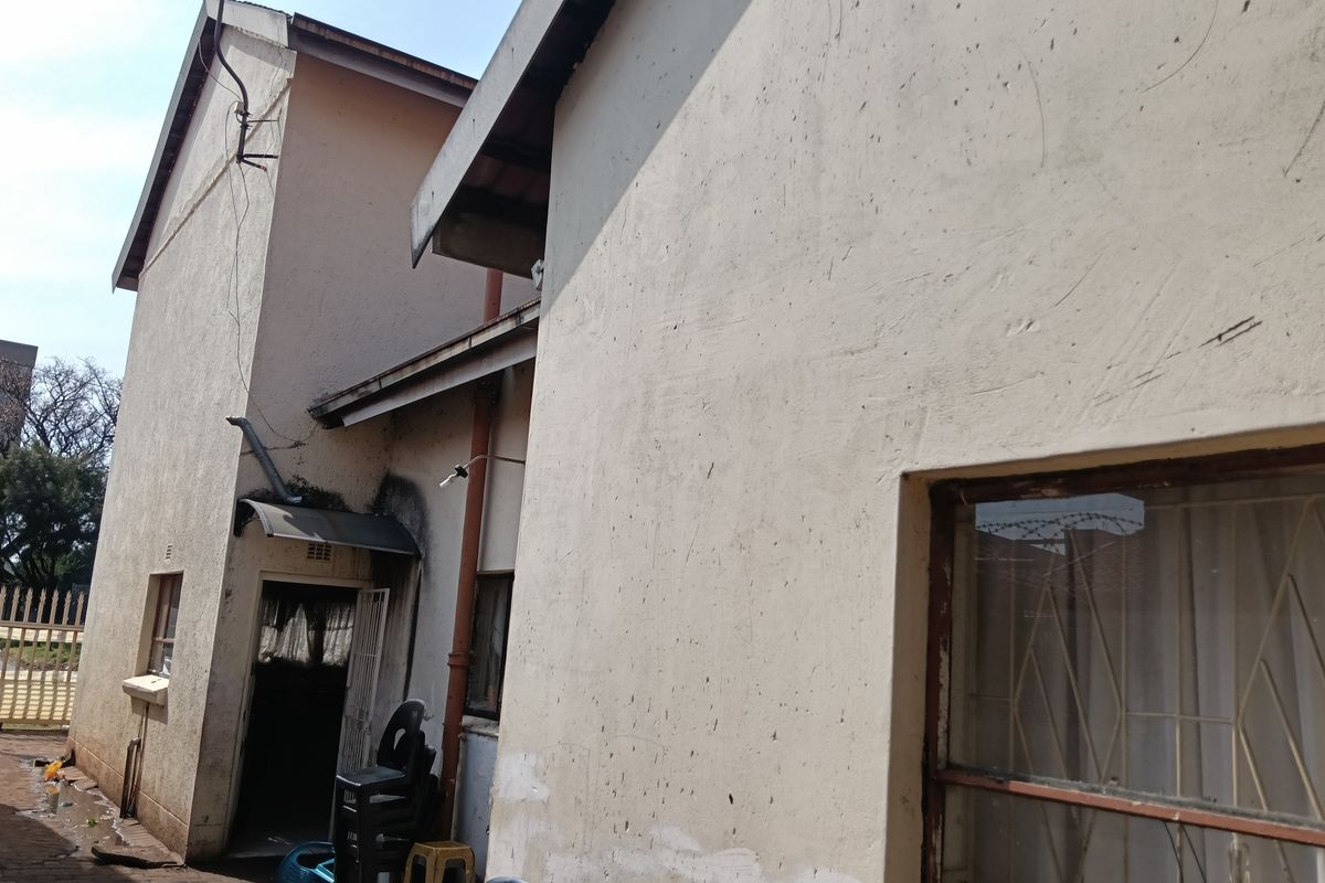 Rear exterior view of the property showing plastered walls, security gates, and window bars, requiring maintenance and exterior painting.