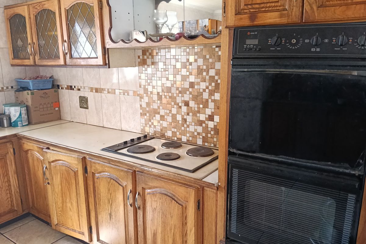A functional kitchen featuring traditional wooden cabinetry, a built-in double oven, an electric hob, and a decorative tiled backsplash.