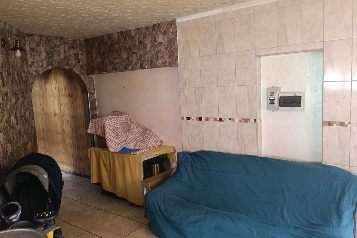 Living area featuring tiled flooring, textured ceiling, and an arched doorway, with wall-mounted electrical distribution board and dated decorative wall tiling.