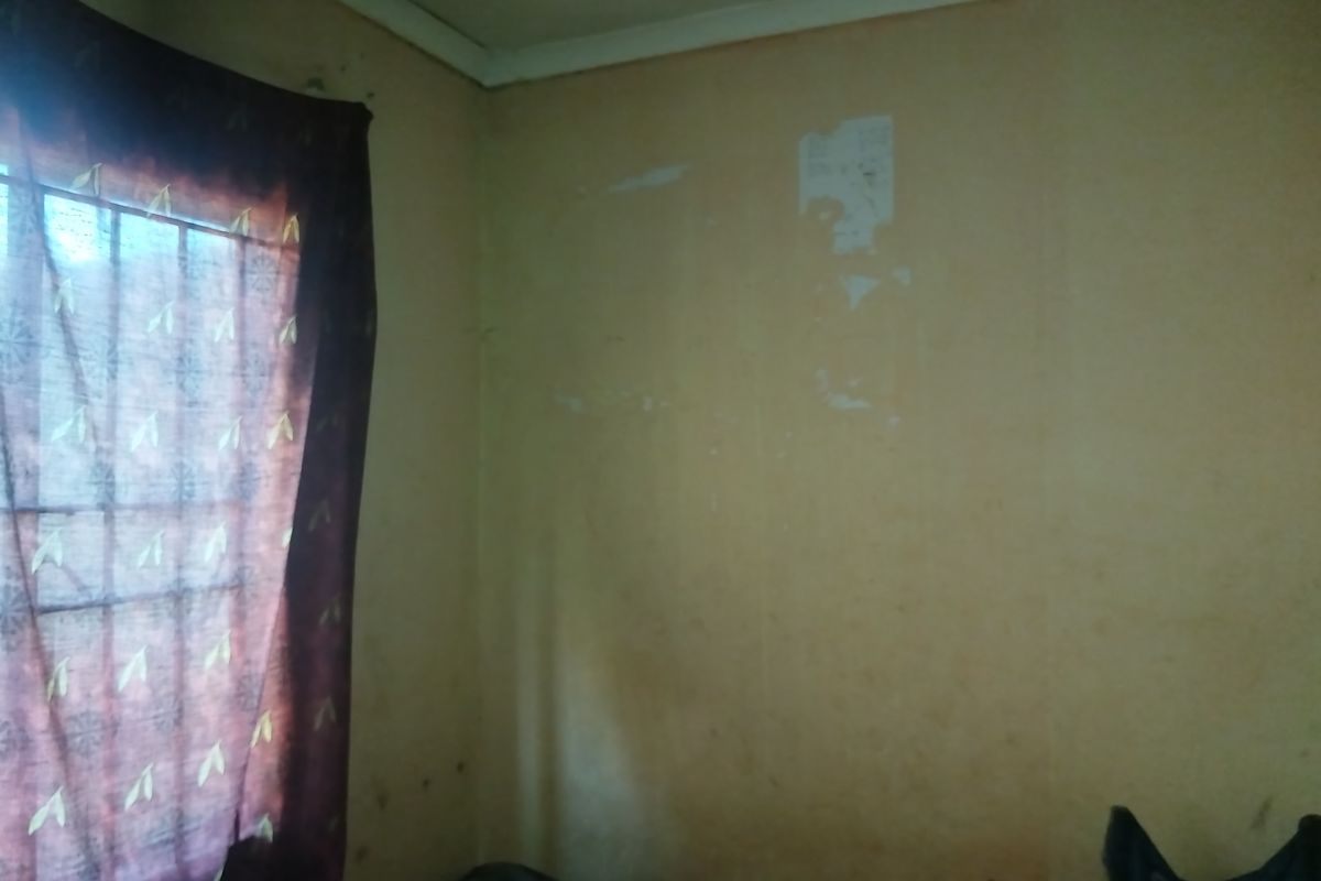 A bedroom interior featuring security bars on the window, showing significant wear to the wall finishes and paintwork requiring maintenance.