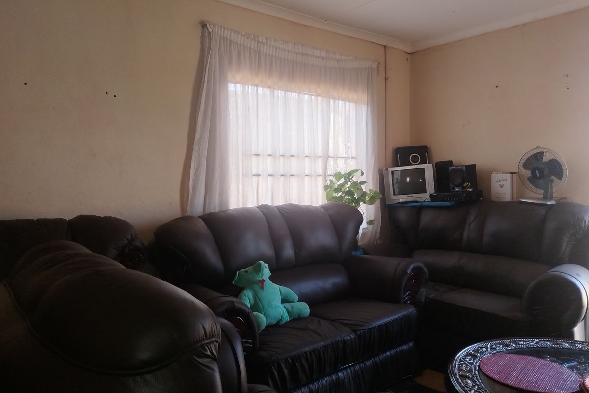 A living room area featuring a window with curtains and plain wall finishes showing signs of wear and minor surface damage.