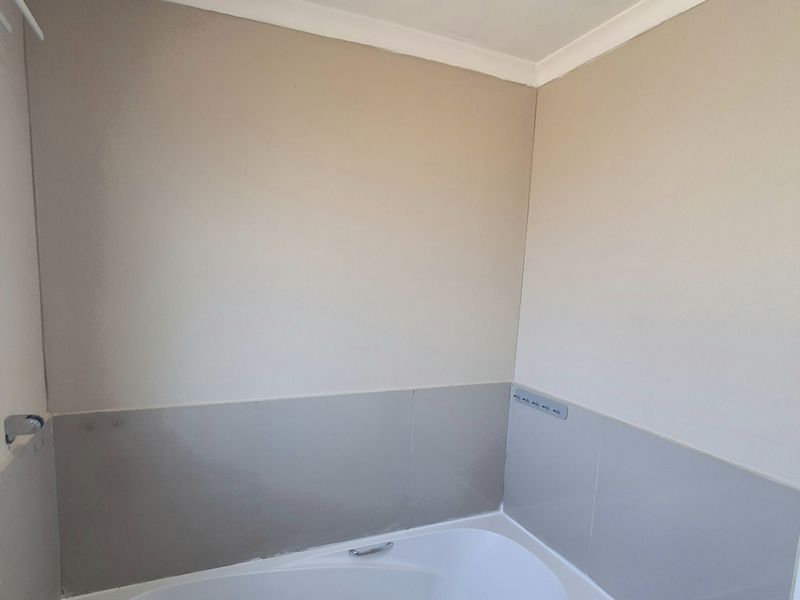 A clean, neutral bathroom featuring a built-in bathtub with tiled splashbacks and chrome fixtures, offering a functional and well-maintained space.
