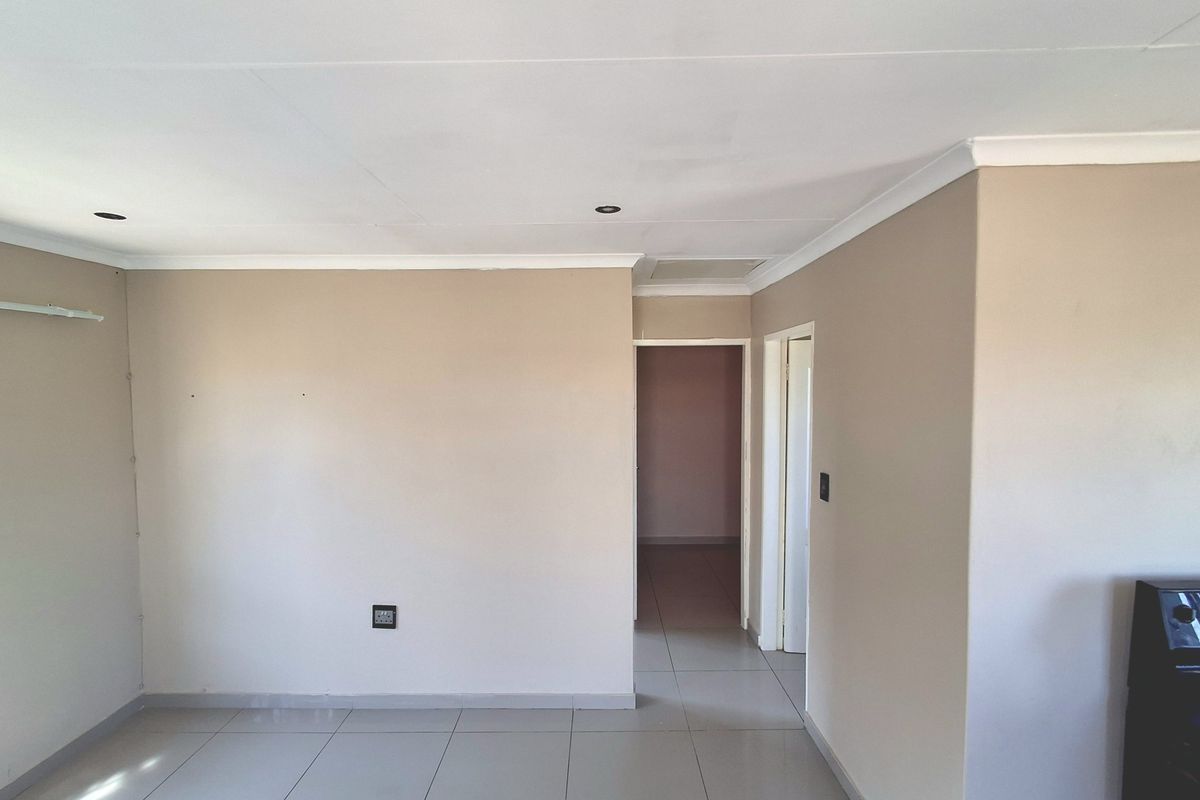An empty living area featuring neutral wall paint, tiled flooring, and recessed downlighting, providing a clean and versatile space for interior design.